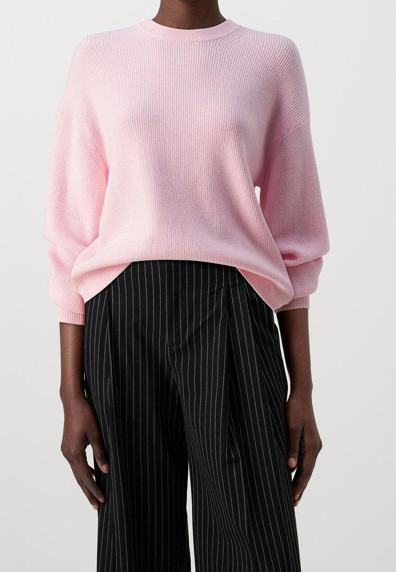 Personne portant un pull côtelé rose clair avec des manches ballon et un pantalon noir taille haute à fines rayures blanches.
