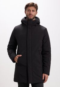 Parka nera con colletto alto e cappuccio removibile, dotata di zip frontale, tasche laterali e un tessuto liscio e texturizzato.