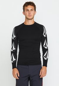Mustapohjainen pitkähihainen rash guard, jossa valkoisia geometrisia kuvioita hihoissa. Venytettävä, istuva muotoilu; sileä pinta, sopii vesitoimintoihin.