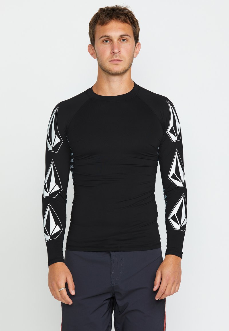 Rash guard de manga larga negro con patrones geométricos blancos en las mangas. Diseño ajustado y elástico; textura suave, adecuado para actividades acuáticas.