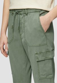 Zelené cargo kalhoty s páskem na stažení v pase, bočními a cargo kapsami a texturovanou tkaninou. Mají prošité švy a uvolněný střih.
