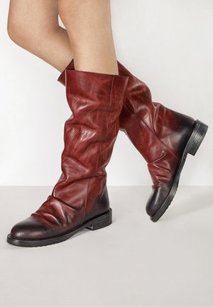 Legs wearing mid-calf, dark red leather boots with black toe and heel accents, flat soles, and slouchy creased texture.