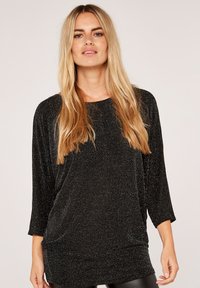 Zwarte, losse top met driekwartmouwen, gemaakt van een glinsterende stof met een subtiel glitters patroon.