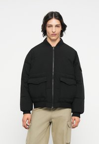 Schwarze Bomberjacke mit Reißverschlussfront, gerippten Bündchen und Saum, ausgestattet mit zwei vorderen aufgesetzten Taschen und gepolstertem Material für Wärme.