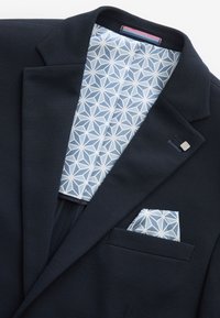 Blazer navy con tejido texturizado, que presenta un forro con un patrón geométrico en azul claro y un pañuelo a juego en el bolsillo del pecho.