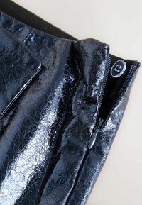 Jachetă din piele ecologică neagră cu un finisaj lucios, având închidere cu fermoar și un buton rotund albastru. Suprafață texturată cu un model crăpat.