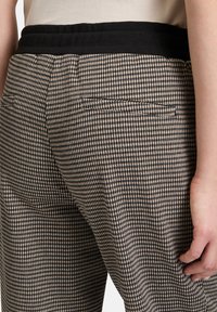 Pantalons à carreaux avec une taille élastique noire, dotés d'une petite poche arrière. Le motif se compose de carrés clairs et foncés alternés.