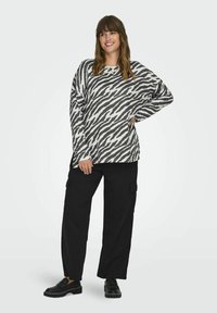 Maglietta a maniche lunghe con un motivo a strisce zebra in bianco e nero, abbinata a pantaloni cargo neri e mocassini neri, su uno sfondo chiaro.