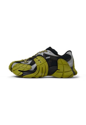 Sneakers with a black mesh upper, metallic silver accents, and green rubber details. Thick, textured sole and prominent design features.
