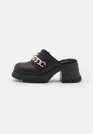 Black clogs with a chunky heel, made of leather-like material, featuring a silver chain accent and a textured rubber sole with tread.