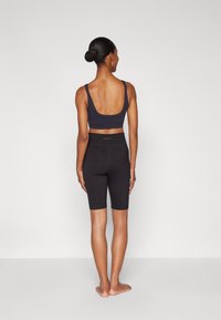 Sort sports-bh med brede stropper, parret med sorte cykelshorts, lavet af et glat, strækbart materiale, tætsiddende design, ingen synlige mønstre.