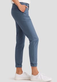 Blue tapered pants made of cotton blend, featuring a smooth texture, side pockets, rolled cuffs, paired with white sneakers.
