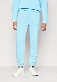 Ljusblå sweatpants gjorda av mjukt bomullsblandat tyg, med elastiska mudd och en elastisk midja, tillsammans med vita sneakers.