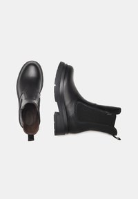 Botas Chelsea de cuero negro con paneles elásticos en los laterales, punta redonda y suela de goma gruesa para mayor tracción. Incluyen una lengüeta para facilitar su colocación.