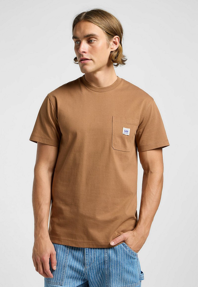 Brun kortärmad t-shirt i bomull med en bröstficka och vit etikett. T-shirten har en avslappnad passform och plana sömmar.