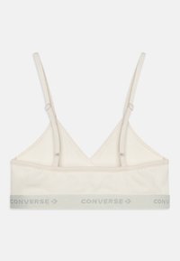 Lys beige bralette med tynne justerbare stropper, en trekantet form, og et logo bånd i lys grå med "CONVERSE" trykt på det.