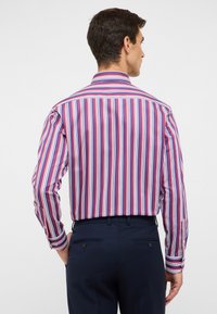 Vista posteriore di un uomo che indossa una camicia a righe multicolori in rosso, blu e bianco, con colletto classico e polsini abbottonati.