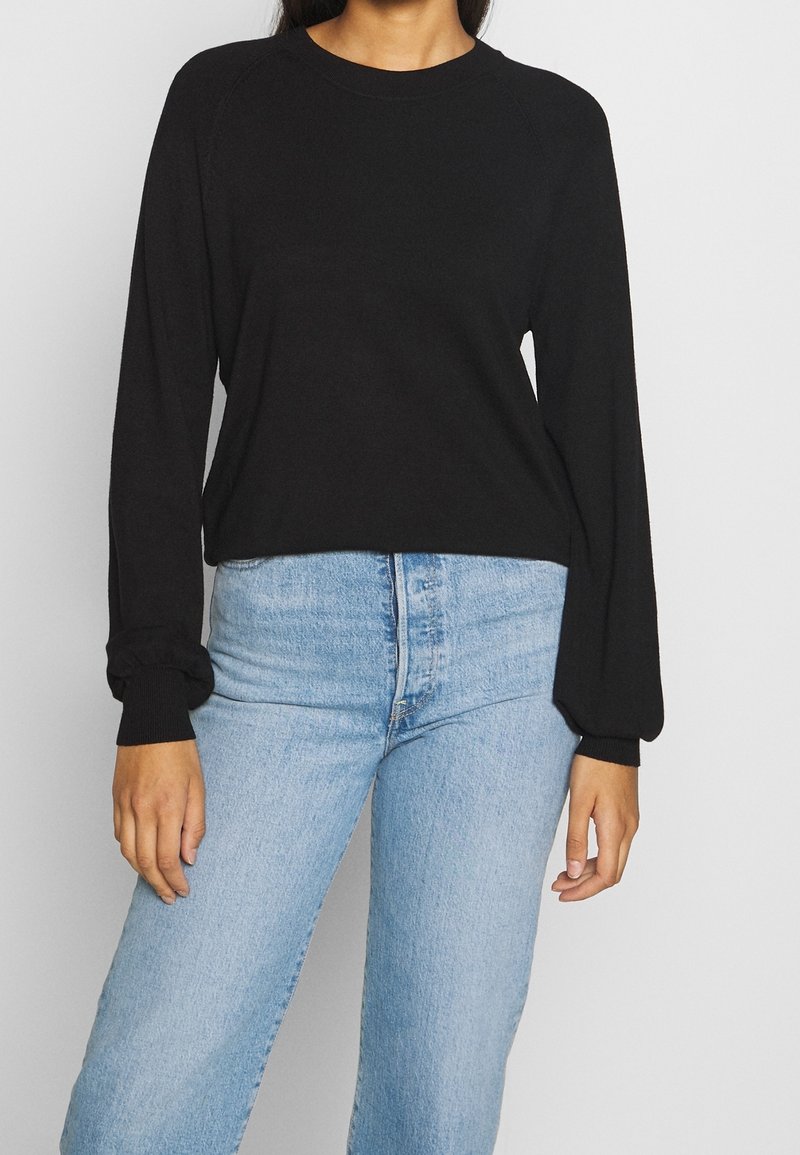 Zwarte lange mouwen crewneck top met geribbelde manchetten, gecombineerd met lichtblauwe high-waisted jeans. De stof lijkt zacht en heeft een minimalistisch ontwerp.