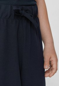 Pantalons texturés bleu marine avec une taille élastique et un nœud noué. Une main à la peau claire repose près de la taille.