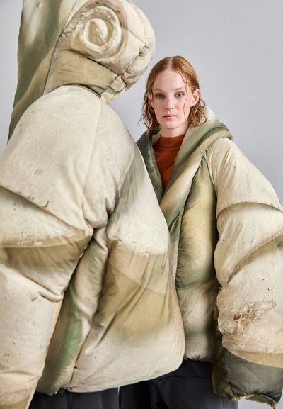 Puffer jacket with oversized silhouette, featuring a light beige and green color scheme, quilted texture, and a prominent hood.