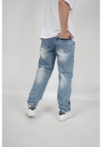 Jeans de mezclilla azul claro con un corte relajado, áreas deslavadas y doble bolsillo trasero. Combinados con zapatillas blancas con detalles en negro.