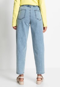 Světle modré džíny s vysokým pasem a volným střihem, se zadními kapsami a nařaseným pasem, doplněné béžovými platformovými sandály.