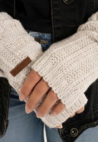 Gebreide vingerloze handschoenen in crème, met ribbelstructuur en een bruin leren label. Warme uitvoering met open vingertoppen voor behendigheid.