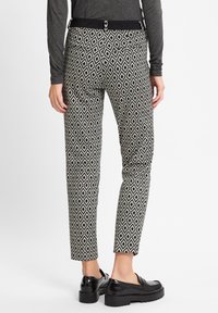 Schwarz-weiße gemusterte Hosen mit einem Rautendesign, schlanker Schnitt, mittelhoher Bund und vier Taschen. Kombiniert mit schwarzen Slippers.