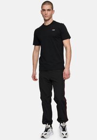 Svart bomulls t-shirt med en liten vit FILA-logotyp. Parat med svarta byxor med röda sidränder och vita sneakers med svarta accenter.