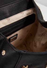 Sac à main en cuir noir avec un intérieur beige à motif logo répété, une poche zippée et des accents métalliques dorés.