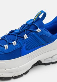 Blue and white Nike sneaker with elastic toggle laces, textured side panel, pull tab with yellow text, and black sole tread.