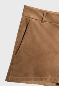 Jupe en daim marron avec une poche latérale et un détail passant de ceinture sur un fond uni clair.