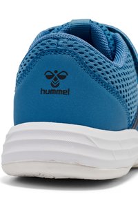 Zapatilla deportiva azul con upper de malla, suela de goma y detalles en gris. Presenta el logo 'hummel' en el talón, tela texturizada y cuello acolchado.