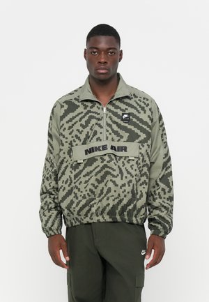 Green pullover jacket featuring a geometric camouflage pattern, elastic waistband, zip neck, and "NIKE AIR" printed across the chest.