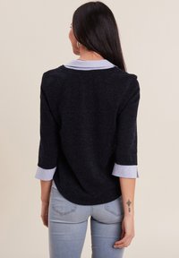 Pull en maille-texturée bleu marine avec une couche à col bleu clair, manches trois-quarts et un ourlet arrondi, associé à un jean bleu clair.