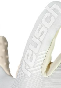 Gant de sport blanc doté d'un matériau texturé, d'un marquage "Reusch" bien en évidence, et d'un design épuré avec des doigts sculptés et une surface adhérente.
