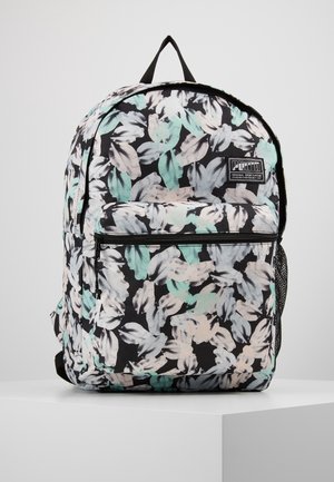 Sac à dos avec motif de feuilles noir, blanc, gris, beige et bleu sarcelle, poche avant zippée, poche latérale en mesh et boucle de transport supérieure sur surface blanche.