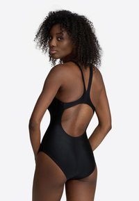 Black one-piece swimsuit with thin straps and an open back design. Smooth texture, athletic fit, and seamless construction.