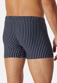 Boxer shorts blu navy con sottili strisce bianche, vita elastica e design aderente. Texture liscia senza loghi o elementi visibili.