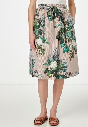 Jupe beige longueur genou à rayures verticales, imprimé floral vert et blanc, ceinture nouée à la taille, associée à des sandales marron à enfiler.