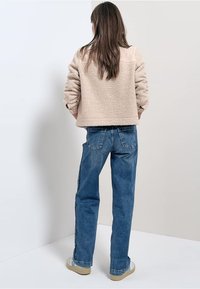 Beige fleece jack met textuurstof, gecombineerd met hoge blauwe denim jeans. Zichtbare stiksels en achterzakken op de jeans.