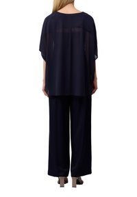 Navy transparente Bluse mit lockerer Passform und kurzen Ärmeln, kombiniert mit weiten navy Hosen. Glatte Textur und minimalistisches Design.