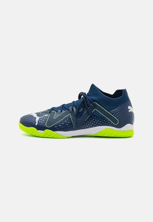 Chaussure de sport montante bleu foncé avec semelle et accents vert néon, logo Puma blanc près des orteils et du talon, et lacets noués au centre.