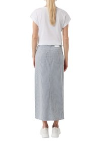 Biała koszulka z krótkim rękawem w zestawie z długą, paskowaną spódnicą. Spódnica charakteryzuje się pionowymi niebieskimi i białymi paskami, ma dwie tylne kieszenie i dopasowaną talię.