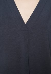 Námořnická modrá v-neck blůza vyrobená z měkké, strukturované látky s detailním řasením. Elegantní design s hladkým povrchem, vhodná pro volnočasové nošení.