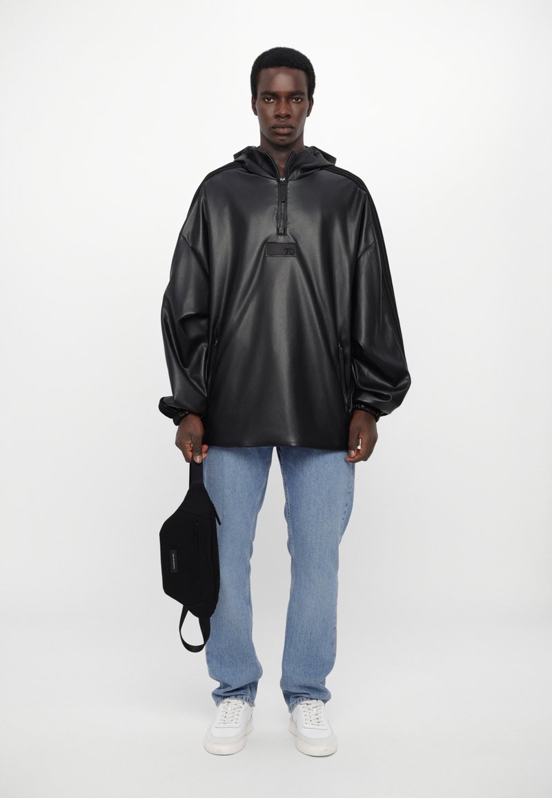 Must värv faux nahast pullover, millel on poolkattega tõmblukk, kapuuts ja eesmine tasku; kantud helesiniste teksade üle. Must vöökott aksessuaarina on kaasas.