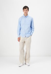 Light blue button-up shirt with a chest pocket, paired with beige trousers and white sneakers. Simple design and soft fabric textures.