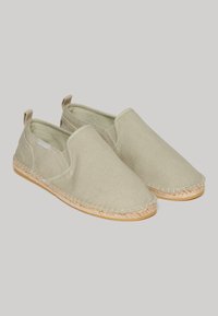 Zapatos slip-on de lona en verde claro con suelas de yute de estilo espadrille trenzadas. Presentan paneles laterales elásticos y una textura suave.