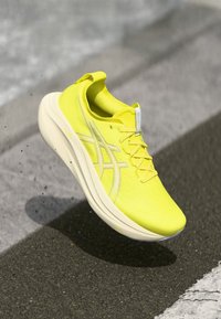 Helle gelbe Sportschuhe mit strukturiertem Obermaterial, abgerundeter weißer Sohle und silbernen Akzenten. Leichtes Design geeignet für das Laufen.