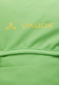 Grön tyg med en strukturerad väv, som har den gula "VAUDE"-logotypen och en enkel design, med en delvis synlig sömdetalj i botten.